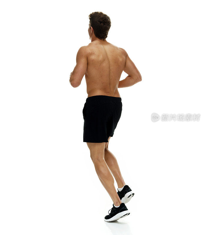 全长/一人/背影/ 20-29岁的成年人英俊的人棕色头发/短发高加索男性/年轻男子跑步/慢跑在白色背景下穿着短裤/跑步短裤/运动鞋/酷的态度